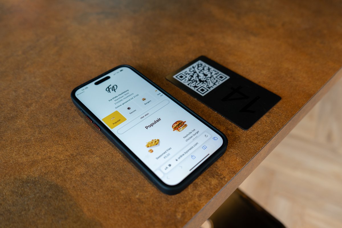 Telefoon met de digitale menukaart van de Online Kiosk naast een QR-tafelkaartje in een horecazaak