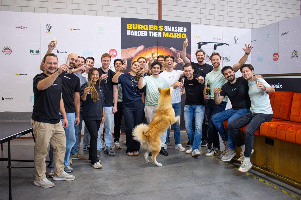 Het Onesix-team proost met champagne in het Onesix-kantoor, met een springende hond op de voorgrond